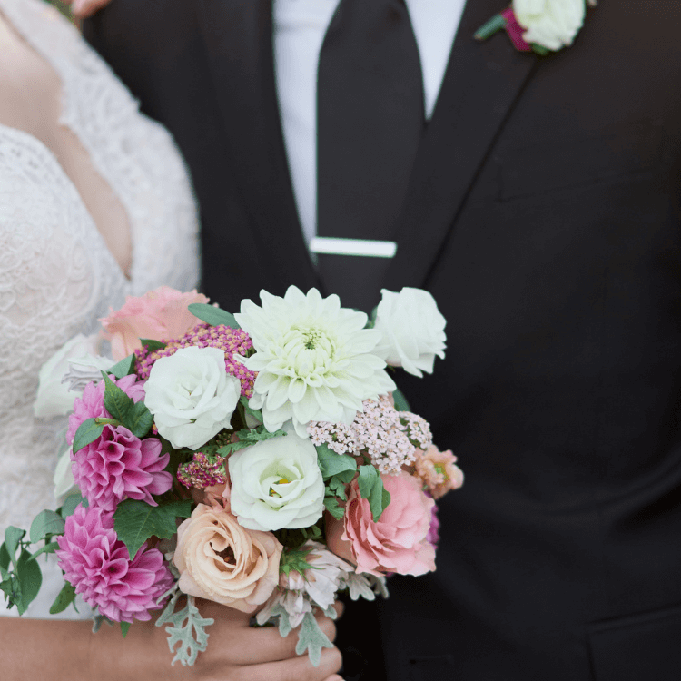 chest shot of bride and groom holding bridal bouquet with rose shaped flowers deahlias and yarrow